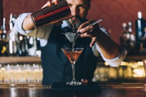barman versa cocktail filtrandolo in bicchiere